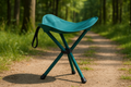 A lightweight, portable folding stool in solid vibrant teal color with sturdy legs, shown in a natural outdoor setting perfect for bird watching